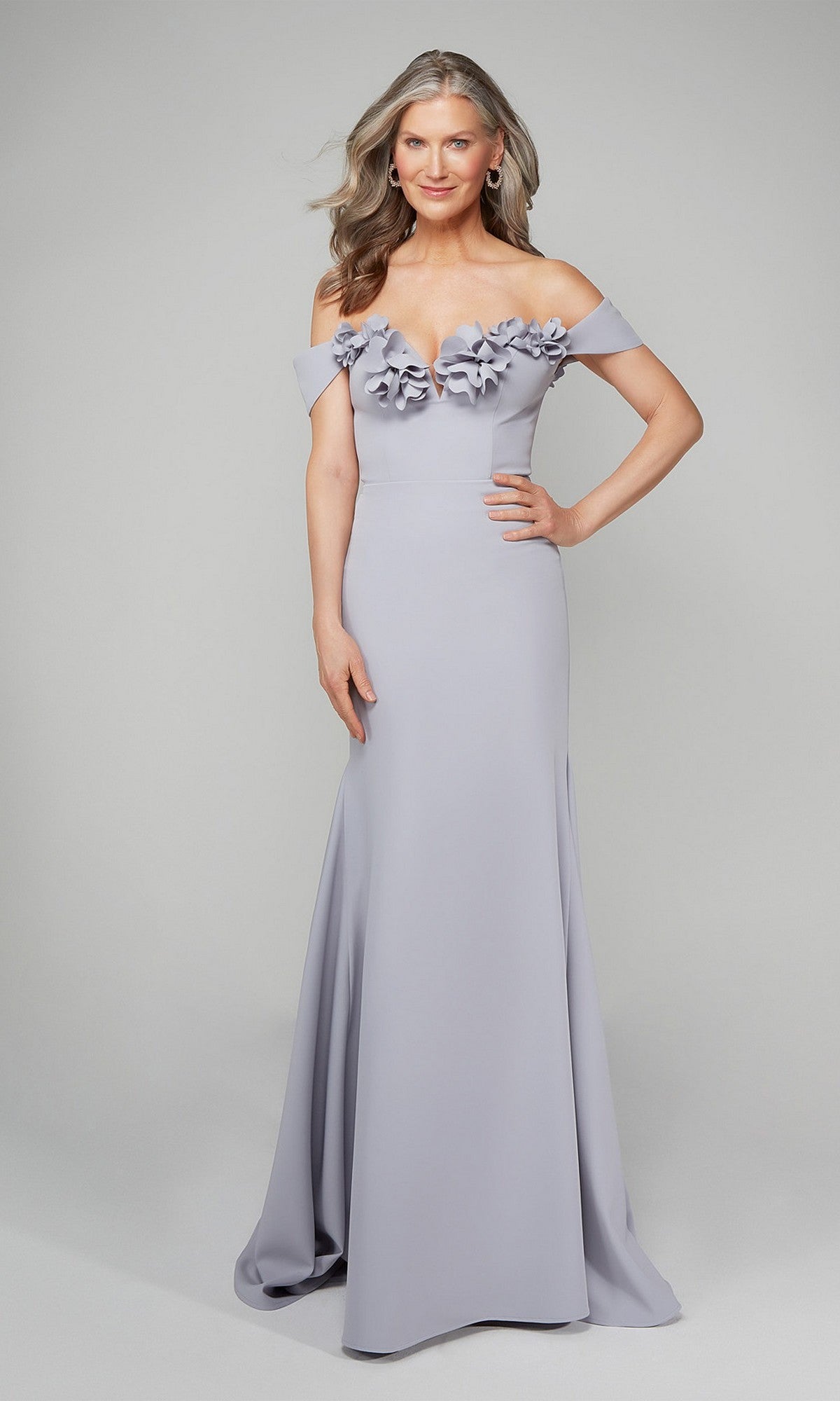 A woman wearing the Alyce 7062 long formal dress in Icelandic Blue, featuring an off-the-shoulder neckline and 3D floral bodice accents, stands against a plain background.